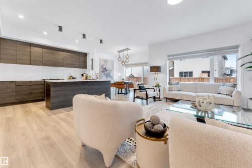 Open-concept living space featuring wood-finish flooring, a contemporary kitchen with dark wood cabinetry and a white subway tile backsplash, and a spacious island with a light-colored countertop - 6203 47 Avenue, Beaumont, AB 