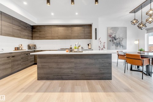 Gourmet kitchen featuring wood-finish cabinetry, a large center island with a light-toned countertop, a white subway tile backsplash, and light wood-finish flooring - 6203 47 Avenue, Beaumont, AB 