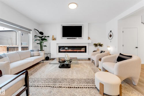 Living area featuring an integrated linear fireplace, light wood-finish flooring, recessed lighting, expansive window, and a contemporary ceiling fixture - 6203 47 Avenue, Beaumont, AB 