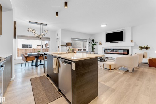 Open-concept living space featuring wood-finish flooring, a kitchen island with stone countertop, stainless steel appliances, and a linear electric fireplace - 6203 47 Avenue, Beaumont, AB 