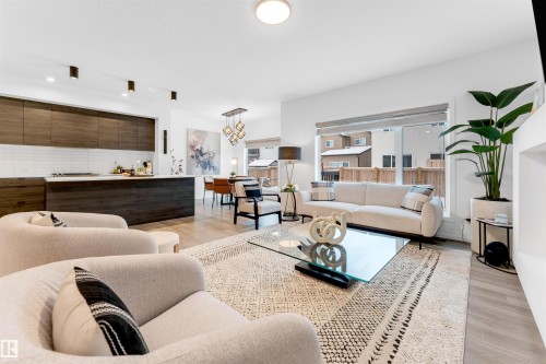 Open-concept living area featuring light wood-finish flooring, a contemporary kitchen with dark wood cabinetry and white subway tile backsplash, and a large window providing ample natural light - 6203 47 Avenue, Beaumont, AB 