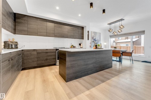 Modern kitchen featuring wood-finish cabinetry, a large center island with a white countertop, and light wood-finish flooring - 6203 47 Avenue, Beaumont, AB 