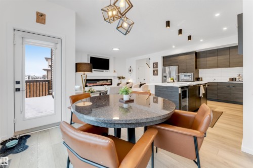 Open concept living space featuring a round granite-finish table, wood-finish flooring, contemporary light fixtures, and a modern kitchen with dark cabinetry and stainless steel appliances - 6203 47 Avenue, Beaumont, AB 