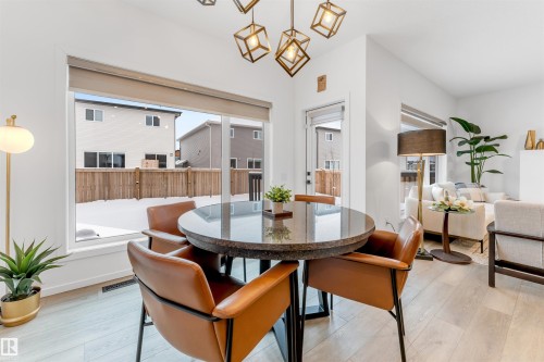 Dining area featuring a large picture window, light wood-finish flooring, and a contemporary chandelier - 6203 47 Avenue, Beaumont, AB 