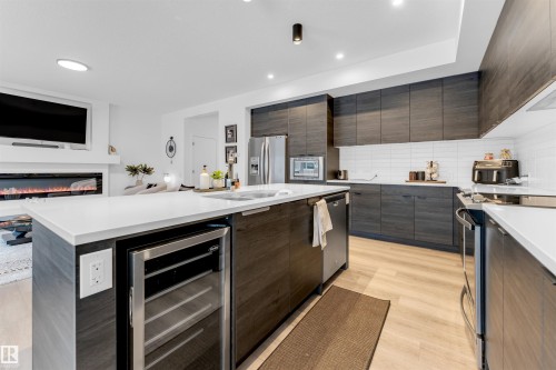 Contemporary kitchen featuring dark wood-finish cabinetry, light countertops, subway tile backsplash, and light wood-finish flooring - 6203 47 Avenue, Beaumont, AB 