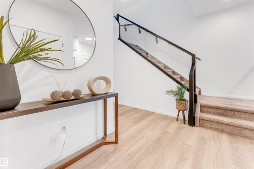 Light wood-finish flooring complements a modern staircase featuring a glass and black metal railing - 6203 47 Avenue, Beaumont, AB 