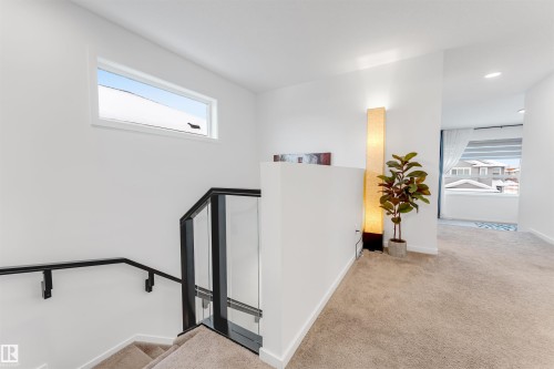 Upper-level landing featuring a contemporary staircase with glass railing and black handrails - 6203 47 Avenue, Beaumont, AB 