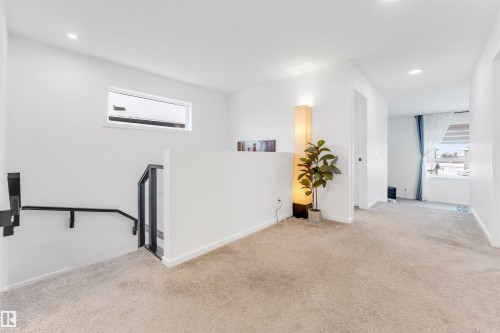 Upper-level hallway with neutral carpeting, recessed lighting, white walls, and a modern black metal and glass railing system - 6203 47 Avenue, Beaumont, AB 