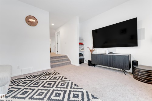 Carpeted living area featuring white walls, a built-in wall-mounted television, and a built-in cabinet - 6203 47 Avenue, Beaumont, AB 