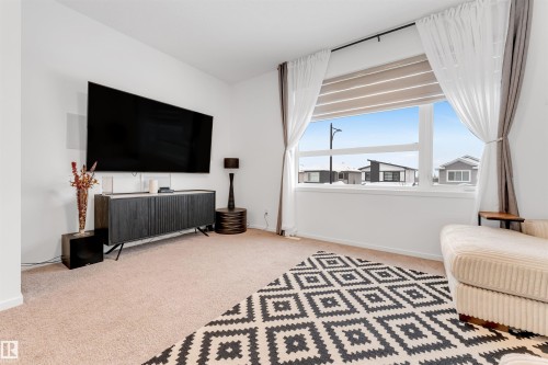Bright living space featuring a large window with roller shades, neutral carpeting, and white walls - 6203 47 Avenue, Beaumont, AB 