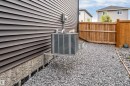 Gravel side yard featuring a wood privacy fence, horizontal plank siding, exposed foundation, and a central air conditioning unit - 6203 47 Avenue, Beaumont, AB 