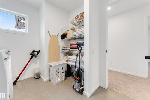 Laundry area featuring ceramic tile flooring, a window with exterior louvered blinds, and a built-in wire shelving system - 6203 47 Avenue, Beaumont, AB 