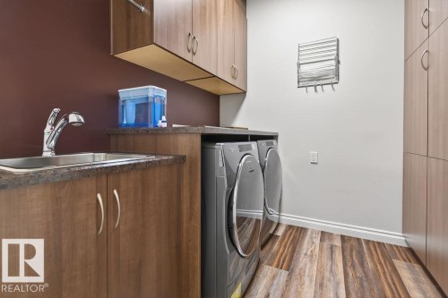 Laundry area featuring wood-finish flooring, built-in cabinetry, a utility sink with a chrome faucet, and a countertop space - 71 Ratelle Circle, St. Albert, AB 