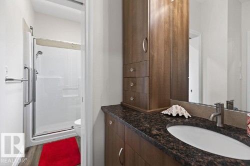 Bathroom featuring a dark wood-finish vanity with an integrated sink, dark speckled countertop, and brushed nickel fixtures - 71 Ratelle Circle, St. Albert, AB 