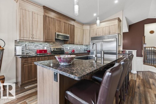Kitchen featuring a large island with a sink and seating, stainless steel appliances, a mosaic tile backsplash, and two-tone cabinetry with upper and lower storage - 71 Ratelle Circle, St. Albert, AB 
