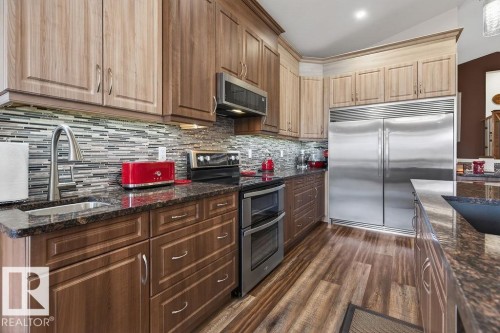 Kitchen featuring wood-finish flooring, two-tone cabinetry, stainless steel appliances, granite countertops, and a mosaic tile backsplash - 71 Ratelle Circle, St. Albert, AB 