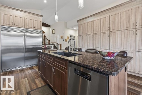 Gourmet kitchen with an oversized central island featuring a dark granite countertop, a built-in sink, and integrated stainless steel dishwasher - 71 Ratelle Circle, St. Albert, AB 