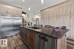 Gourmet kitchen with an oversized central island featuring a dark granite countertop, a built-in sink, and integrated stainless steel dishwasher - 