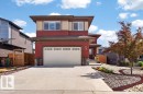 Contemporary two-story residence featuring a striking red and beige exterior, a concrete driveway, an integrated garage with decorative windows, and a landscaped front yard with decorative rock and a mature tree - 71 Ratelle Circle, St. Albert, AB 