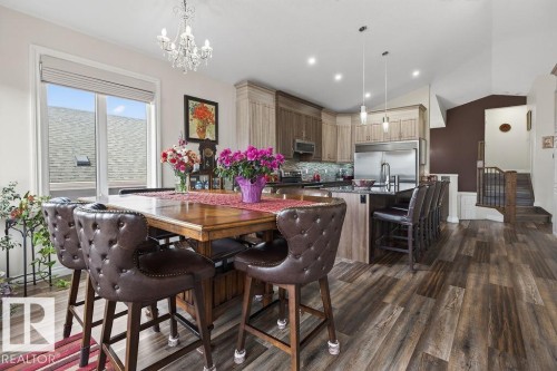 Open-concept kitchen and dining area featuring wood-finish flooring, a kitchen island with seating, pendant lighting, and stainless steel appliances - 71 Ratelle Circle, St. Albert, AB 