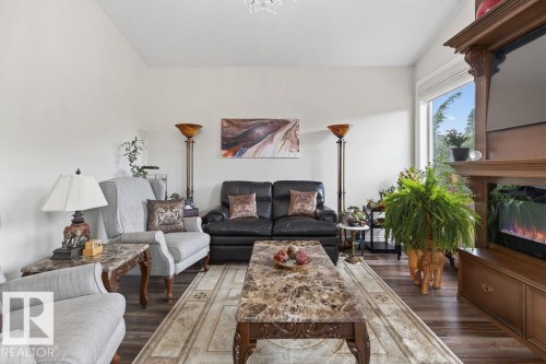 Bright living area featuring wood-finish flooring, a decorative chandelier, and a built-in entertainment center with an electric fireplace - 71 Ratelle Circle, St. Albert, AB 
