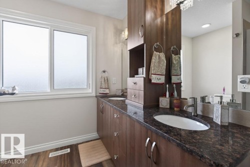 Dual undermount sinks set into a dark speckled countertop, complemented by wood-finish cabinetry - 71 Ratelle Circle, St. Albert, AB 