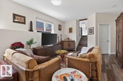 Spacious living area featuring wood-finish flooring, a contemporary ceiling light fixture, and a white interior door with paneling - 