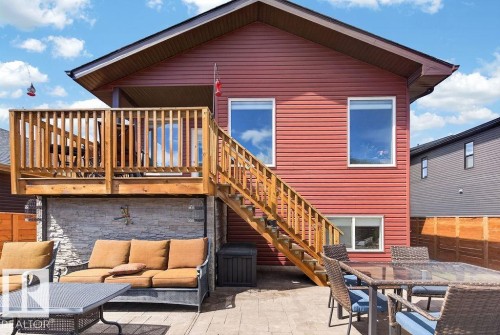 Exterior featuring red horizontal siding, a two-level wood deck with stairs, a ground-level patio, and a stone-clad foundation accent - 71 Ratelle Circle, St. Albert, AB 