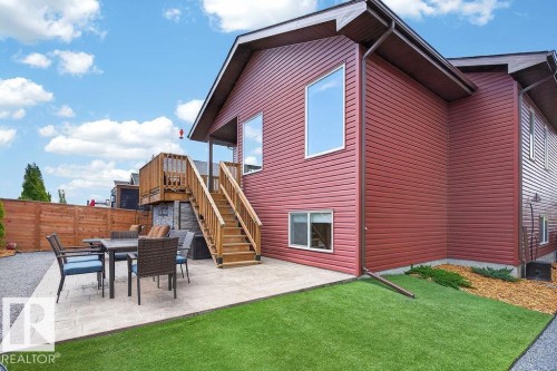 Red horizontal siding exterior featuring a multi-level wooden deck, a ground-level paver patio, a fenced perimeter, and an artificial turf area - 71 Ratelle Circle, St. Albert, AB 