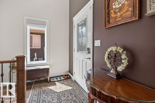 Entryway featuring wood-finish flooring, a white paneled door with leaded glass, a built-in window bench, and a dark wood handrail with black iron spindles - 71 Ratelle Circle, St. Albert, AB 