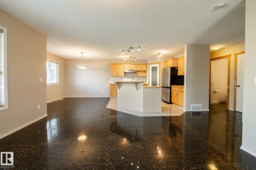 Open-concept living space featuring dark, polished flooring, a kitchen island with seating, natural wood cabinetry, and stainless steel appliances - 55 Lamplight Cove, Spruce Grove, AB - Indoor Photo Showing Kitchen