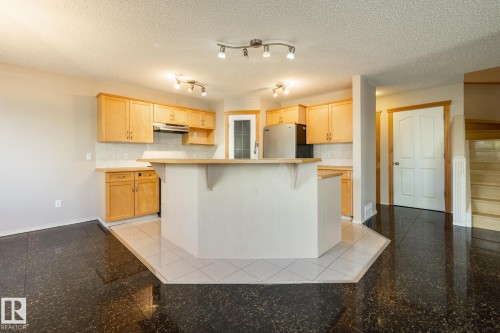 Kitchen featuring light wood-finish cabinetry, a white tile backsplash, an integrated breakfast bar, and stainless steel appliances - 55 Lamplight Cove, Spruce Grove, AB - Indoor Photo Showing Kitchen
