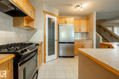 Kitchen featuring light wood cabinetry, stainless steel appliances, tiled flooring, and a tiled backsplash - 55 Lamplight Cove, Spruce Grove, AB - Indoor Photo Showing Kitchen With Stainless Steel Kitchen