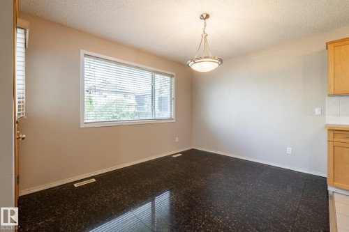 Spacious room featuring dark patterned flooring, a large window with blinds, and neutral wall tones - 55 Lamplight Cove, Spruce Grove, AB - Indoor