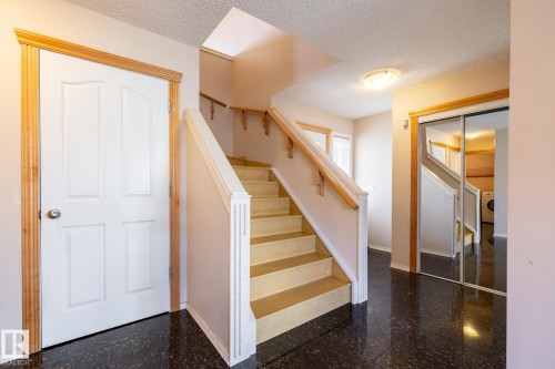Entry foyer featuring dark polished flooring, a white paneled door with natural wood trim, and a staircase with light-colored treads and a natural wood handrail - 55 Lamplight Cove, Spruce Grove, AB - Indoor Photo Showing Other Room