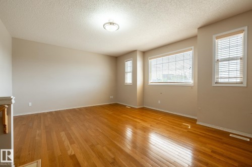 Spacious room featuring wood-finish flooring, neutral-toned walls, multiple windows with blinds, and a ceiling-mounted light fixture - 55 Lamplight Cove, Spruce Grove, AB - Indoor Photo Showing Other Room