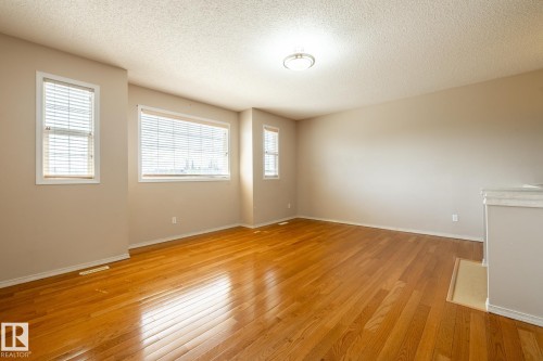 Spacious room featuring wood-finish flooring, neutral-toned walls, multiple windows with blinds, and a flush-mount ceiling light fixture - 55 Lamplight Cove, Spruce Grove, AB - Indoor Photo Showing Other Room