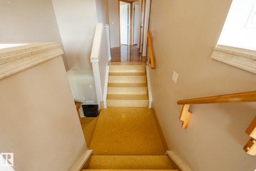 Carpeted staircase with wood handrails, light beige wall paint, and white trim accents - 55 Lamplight Cove, Spruce Grove, AB - Indoor Photo Showing Other Room