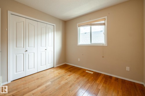 Interior room featuring wood-finish flooring, a white-framed window with a bamboo shade, and a bi-fold closet with panel doors and silver-tone hardware - 55 Lamplight Cove, Spruce Grove, AB - Indoor Photo Showing Other Room
