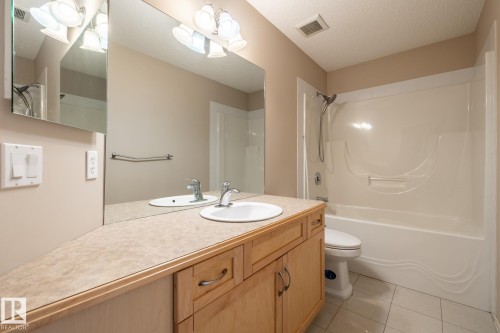 Bathroom featuring a light wood-finish vanity with two inset sinks, a large wall-mounted mirror, a matching countertop, and a white tub/shower combination with a curved surround - 55 Lamplight Cove, Spruce Grove, AB - Indoor Photo Showing Bathroom