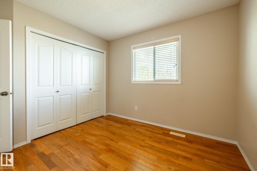Hardwood flooring complements neutral wall tones in this room featuring a double bi-fold closet and a window with horizontal blinds - 55 Lamplight Cove, Spruce Grove, AB - Indoor Photo Showing Other Room