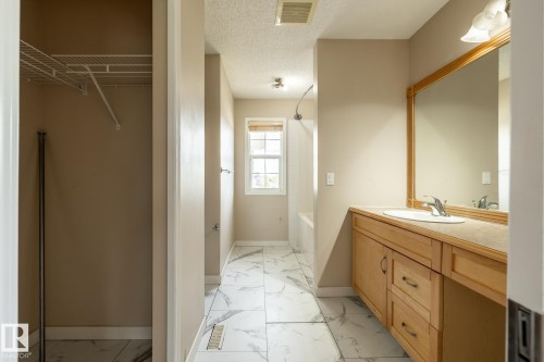 Bathroom featuring light-toned cabinetry with an integrated sink, a large framed mirror, a separate tub/shower combination, and white tile flooring with gray veining - 55 Lamplight Cove, Spruce Grove, AB - Indoor Photo Showing Bathroom