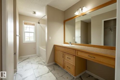 Bathroom featuring a light wood-finish vanity with integrated sink, expansive wall-mounted mirror, and a combination tub and shower - 55 Lamplight Cove, Spruce Grove, AB - Indoor Photo Showing Bathroom