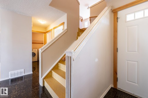 Foyer featuring a white paneled front door with transom windows, dark speckled flooring, and a staircase with white risers and light-toned treads - 55 Lamplight Cove, Spruce Grove, AB - Indoor Photo Showing Other Room