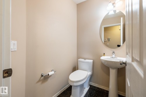Pedestal sink with chrome faucet, circular mirror, and wall-mounted light fixture - 55 Lamplight Cove, Spruce Grove, AB - Indoor Photo Showing Bathroom