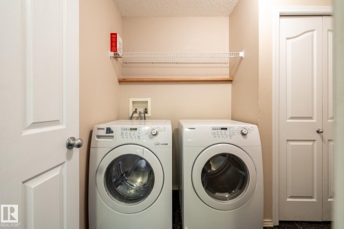 Dedicated laundry space featuring a side-by-side washer and dryer, an overhead wire shelf, and a wood plank shelf - 55 Lamplight Cove, Spruce Grove, AB - Indoor Photo Showing Laundry Room