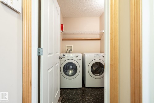Dedicated laundry area featuring a dark stone-look flooring, white appliances, and a mounted wire shelf with a wood support - 55 Lamplight Cove, Spruce Grove, AB - Indoor Photo Showing Laundry Room