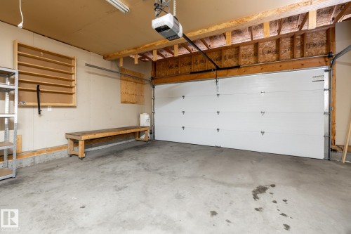Spacious garage featuring a concrete floor, overhead lighting, an automatic garage door opener, and exposed wood ceiling joists - 55 Lamplight Cove, Spruce Grove, AB - Indoor Photo Showing Garage