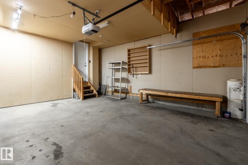 Spacious garage featuring a concrete floor, exposed wood ceiling joists, and a built-in wooden workbench - 55 Lamplight Cove, Spruce Grove, AB - Indoor Photo Showing Garage
