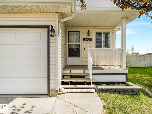 Front exterior featuring a white garage door, light-colored siding, a covered porch with white railings, and a stone-faced planter box - 2921 23 Street, Edmonton, AB 